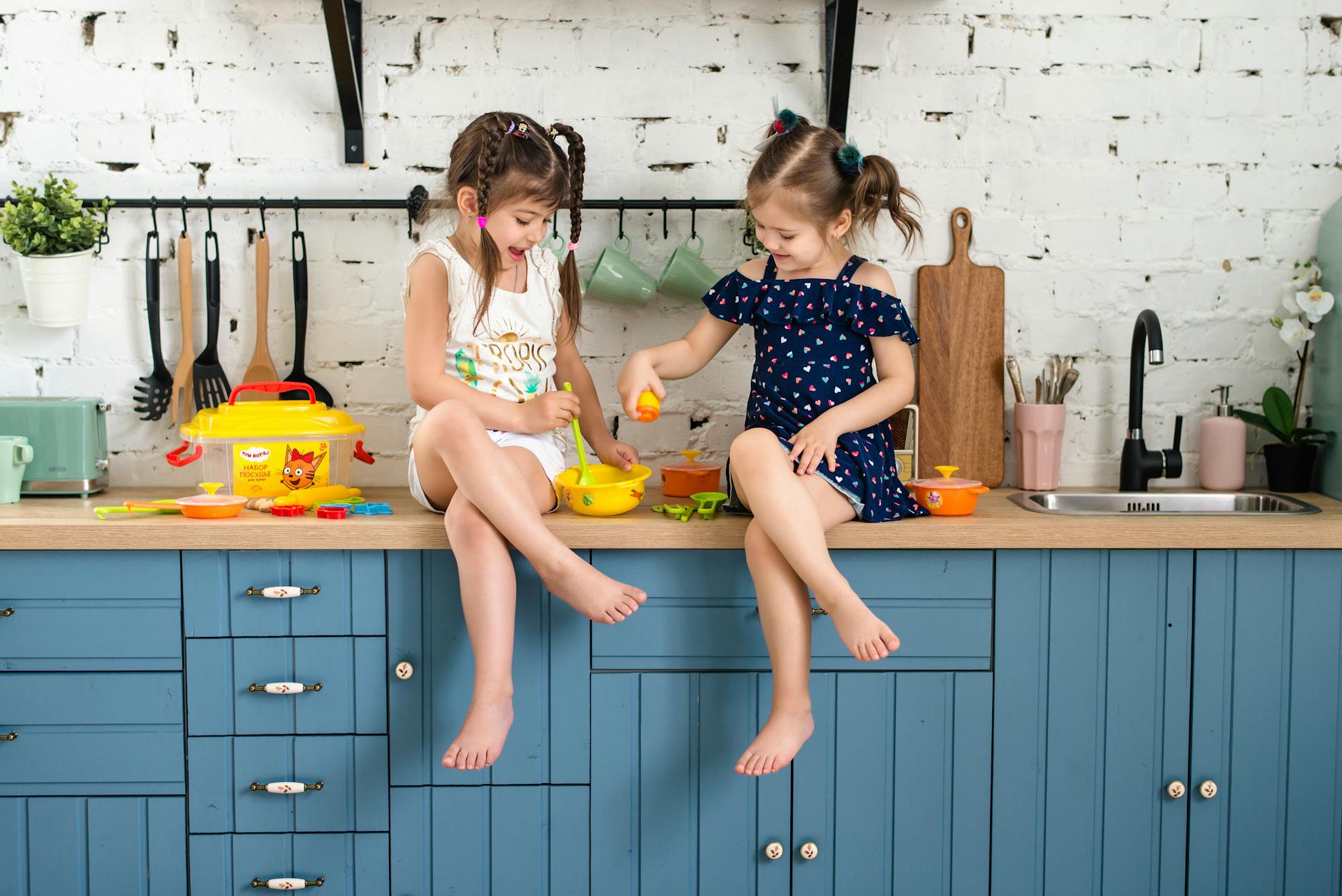 two girls sitting on a kitchen counter playing with plastic toys